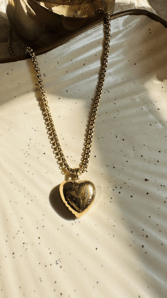 Gold heart-shaped pendant necklace on a textured white surface