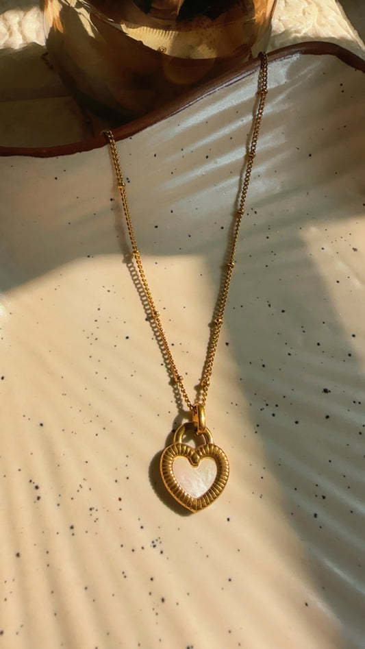 Gold necklace with a heart-shaped pendant on a textured beige surface