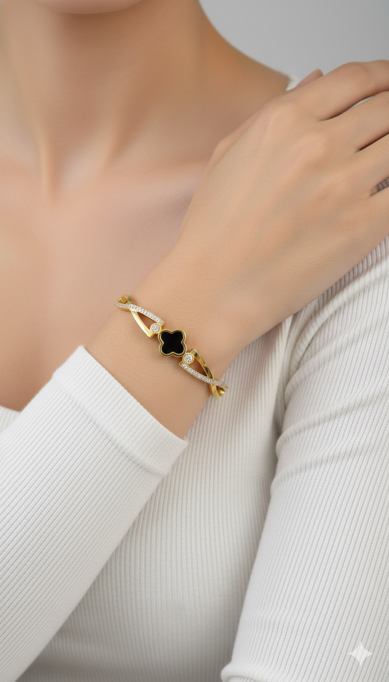Gold black clover bracelet with a black gemstone on a person's wrist against a neutral background
