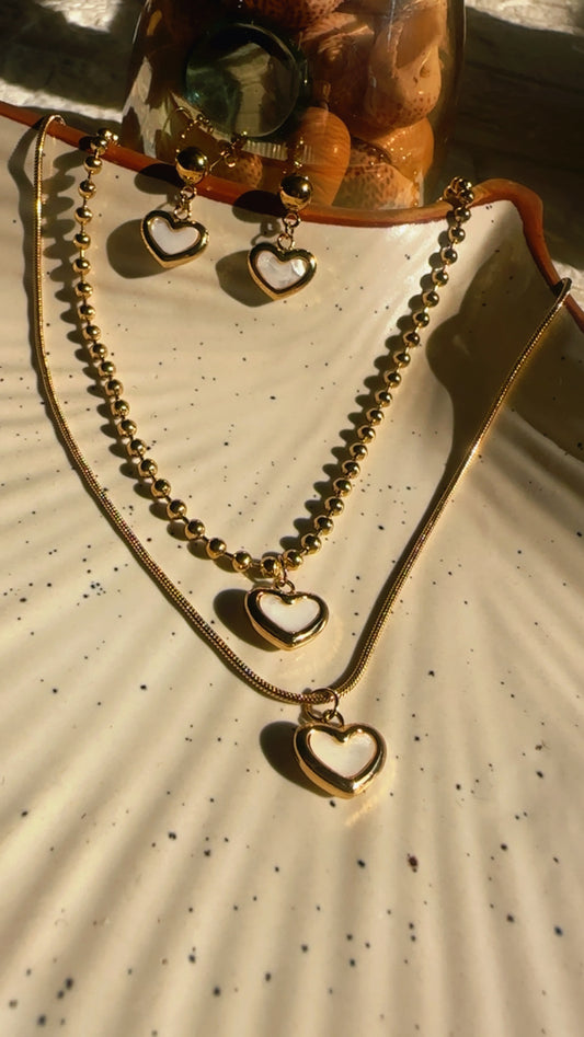 Gold necklace with heart-shaped pendants on a textured beige surface