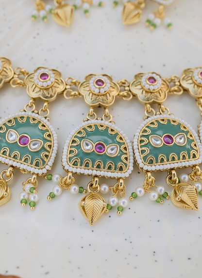 Gold and green jewelry piece with pink stones on a light background