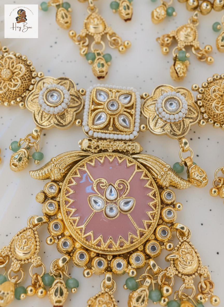 Gold jewelry set with pink center and green beads on a white background