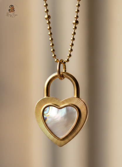 Gold heart-shaped lock necklace with a clear heart inlay on a blurred beige background