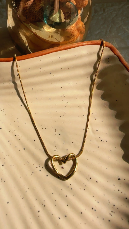 Gold necklace with a heart-shaped pendant on a textured surface