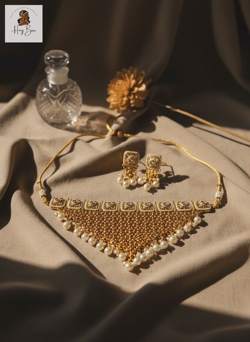 Gold necklace and earrings on a textured surface with a bottle and flower decor.