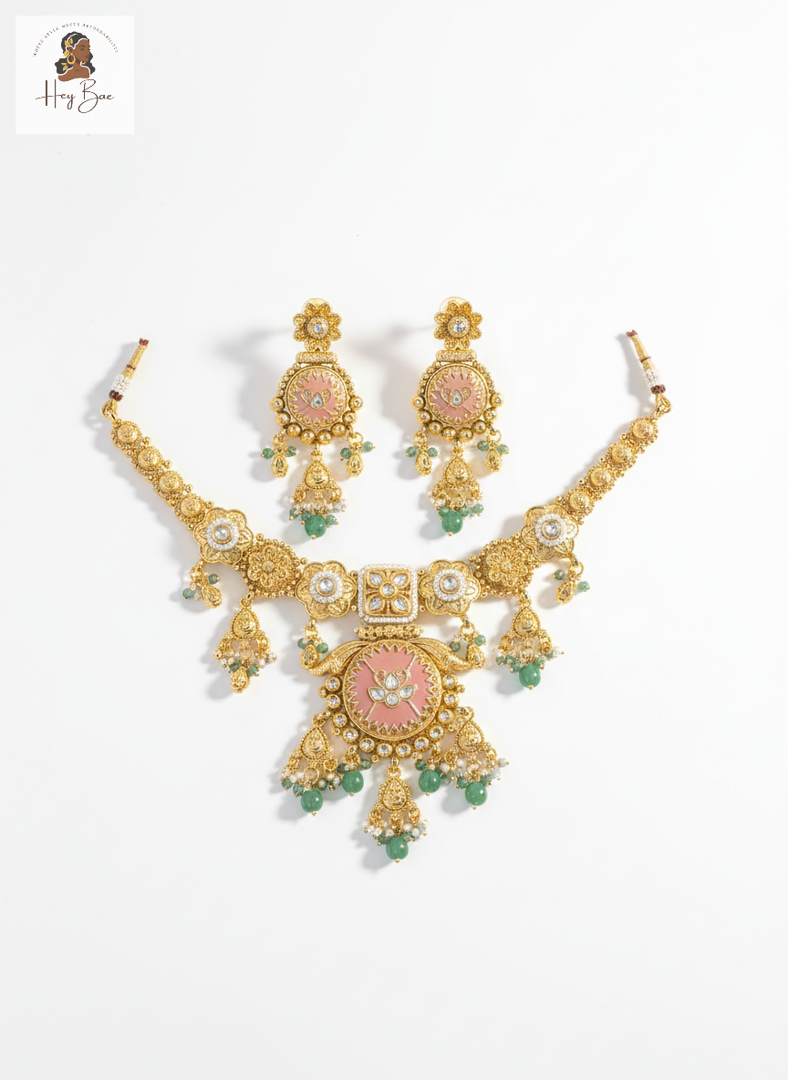 Gold necklace and earrings set with pink and green stones on a white background