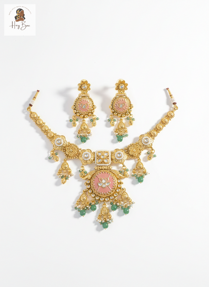 Gold necklace and earrings set with pink and green stones on a white background