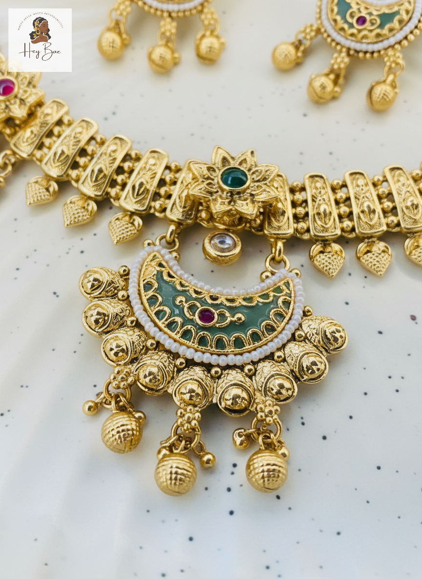 Gold necklace with intricate design and colorful stones on a light background