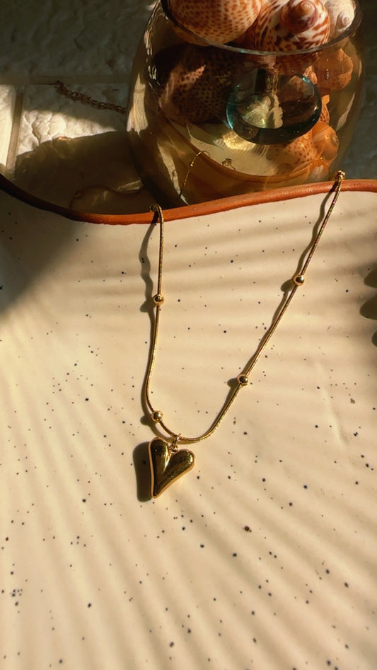 Gold necklace with a heart pendant on a textured surface