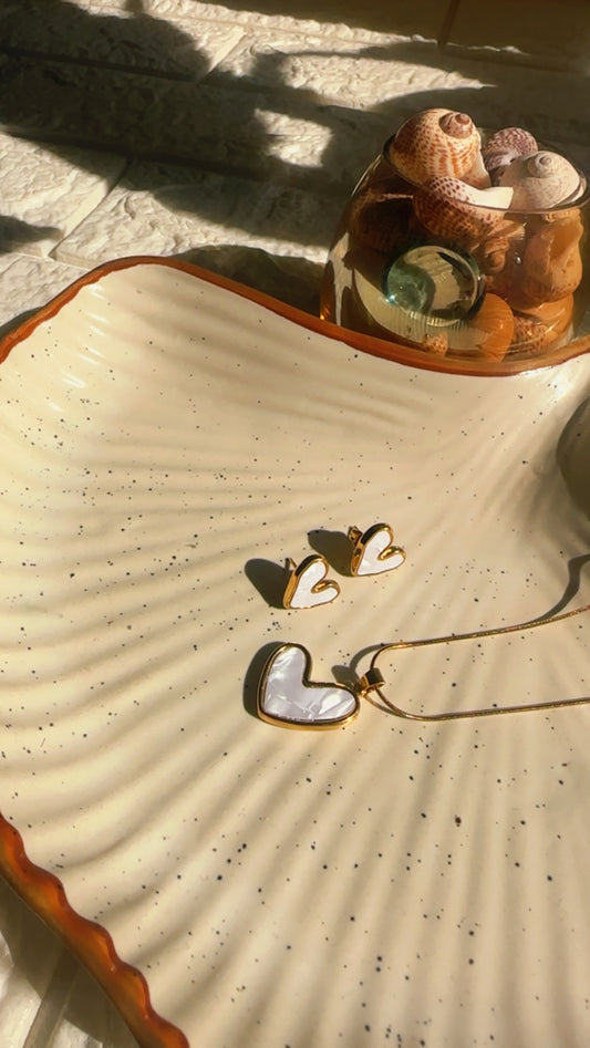 Heart-shaped earrings on a textured surface with a shell and small objects in the background.
