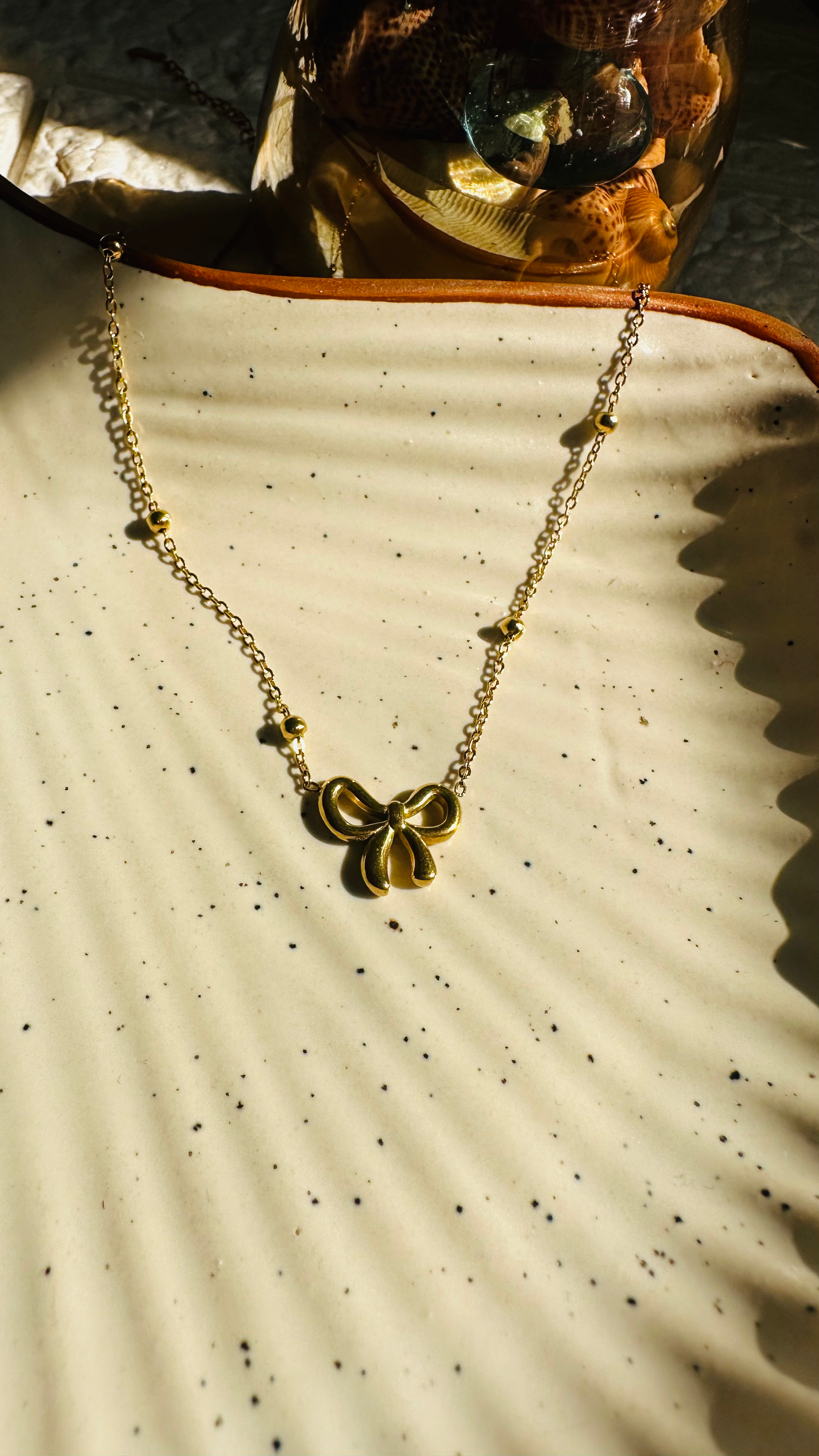 Gold necklace with a butterfly pendant on a textured beige surface