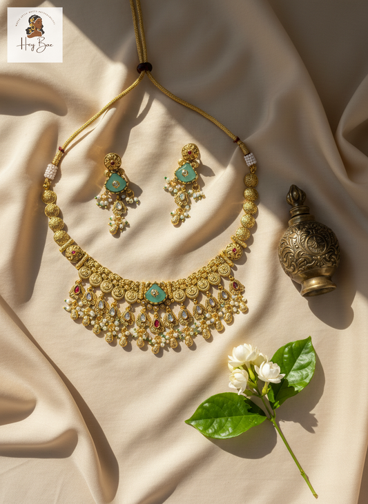 Gold necklace and earrings set with a decorative bottle and flowers on a beige fabric background