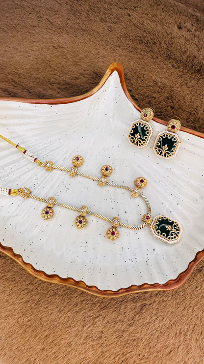  Hey Bae antique gold finish necklace set with emerald green and ruby stones on a decorative plate with a brown background