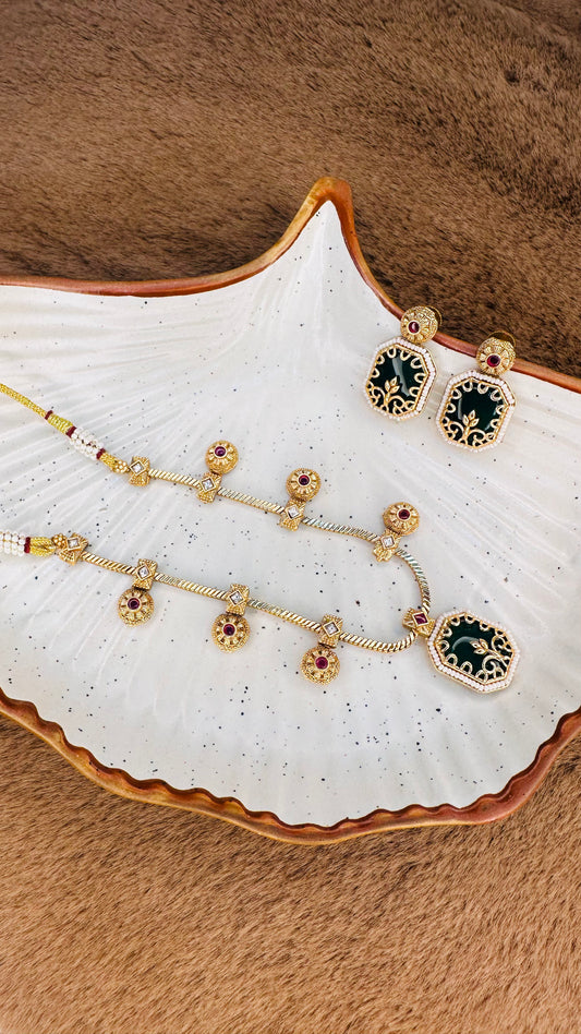  Hey Bae antique gold finish necklace set with emerald green and ruby stones on a decorative plate with a brown background