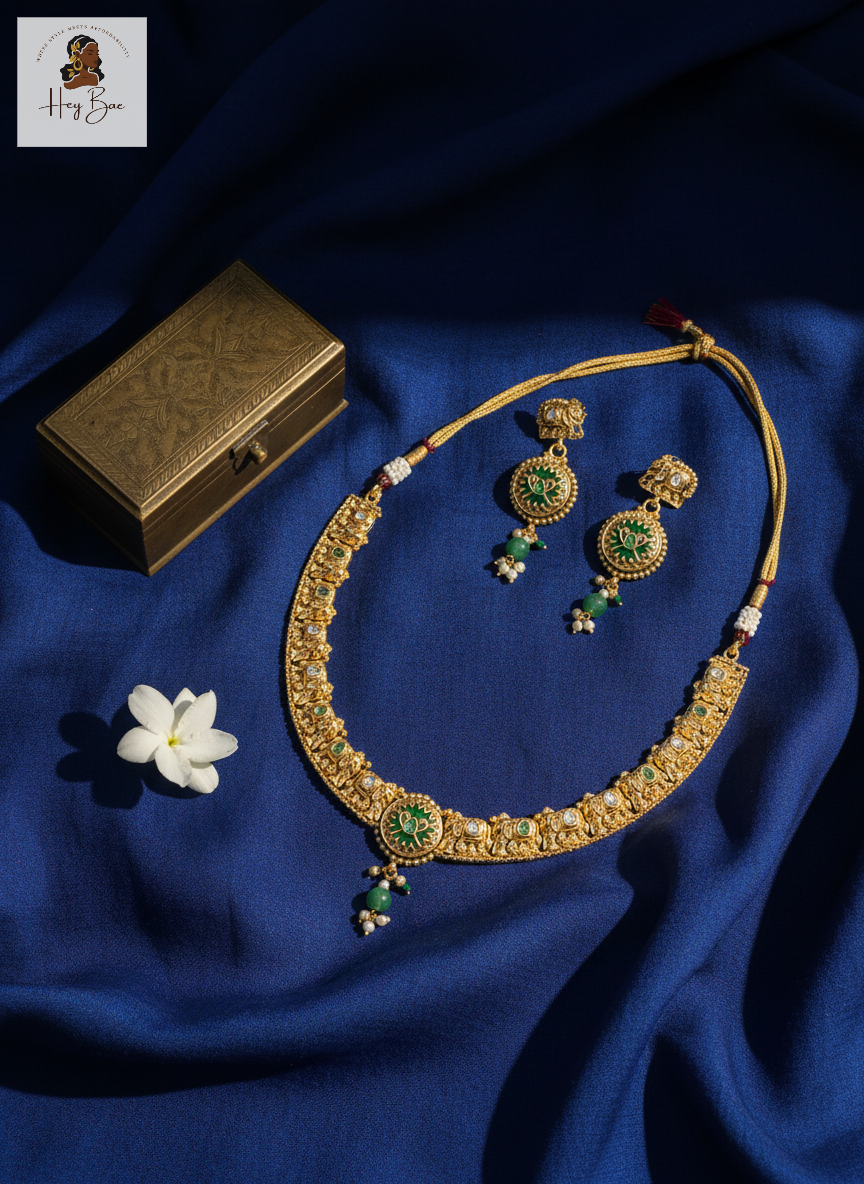 Gold necklace with green stones and matching earrings on a blue fabric background