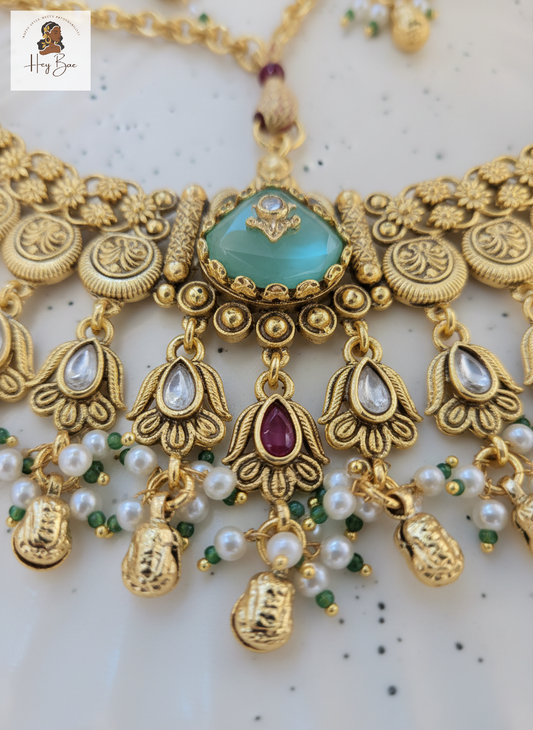 Ornate gold Hey Bae antique gold necklace set with mint green stones drops on a light background