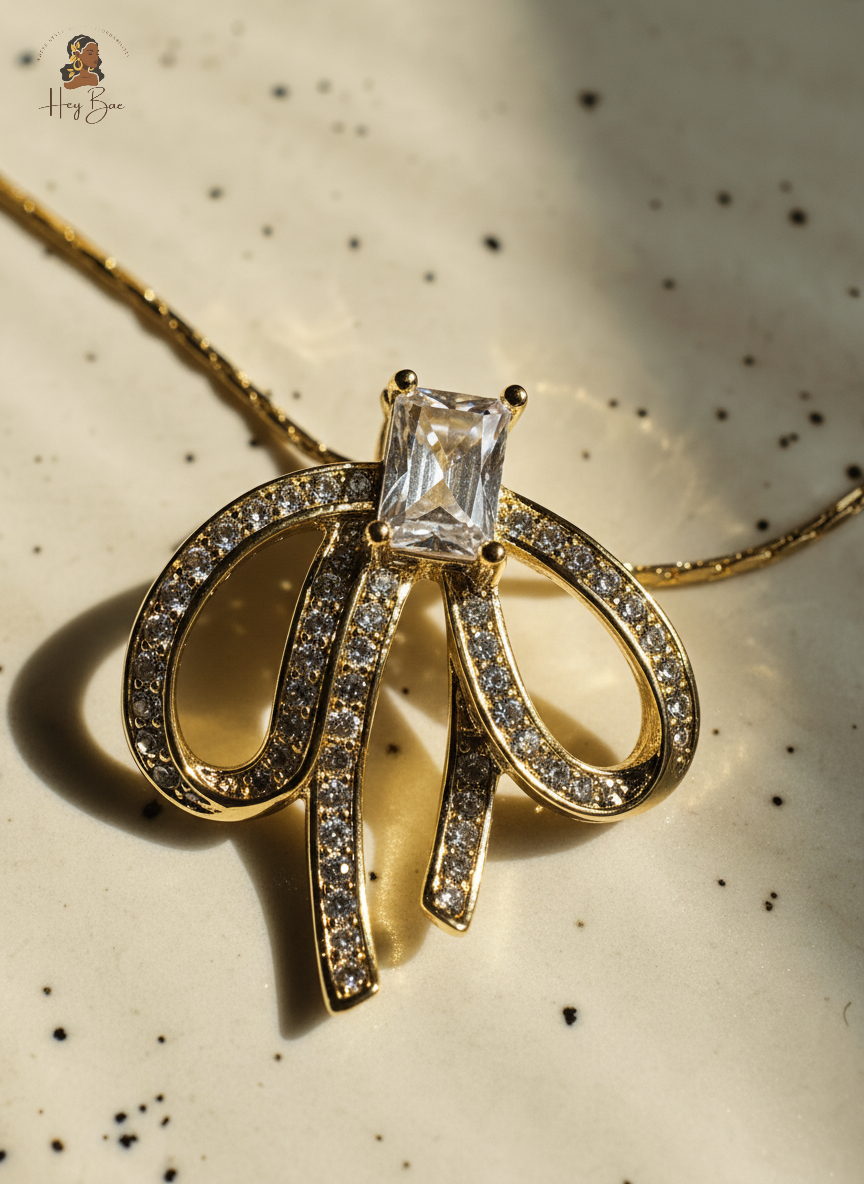 Gold necklace with a bow design and central gemstone on a speckled background