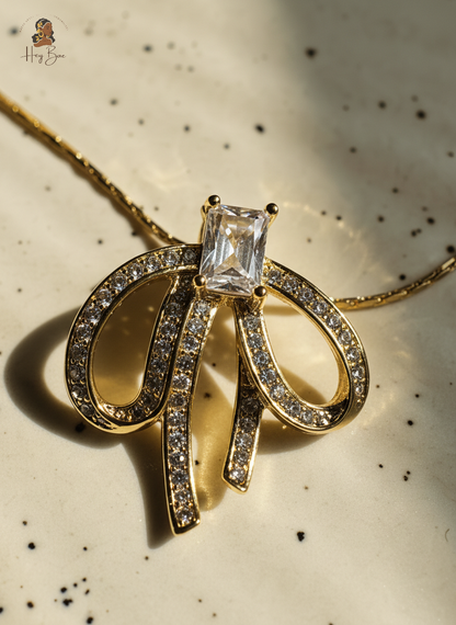 Gold necklace with a bow design and central gemstone on a speckled background