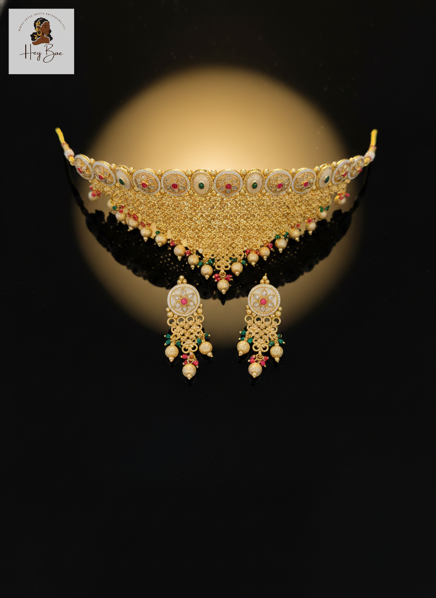 Ornate gold necklace with matching earrings on a reflective surface