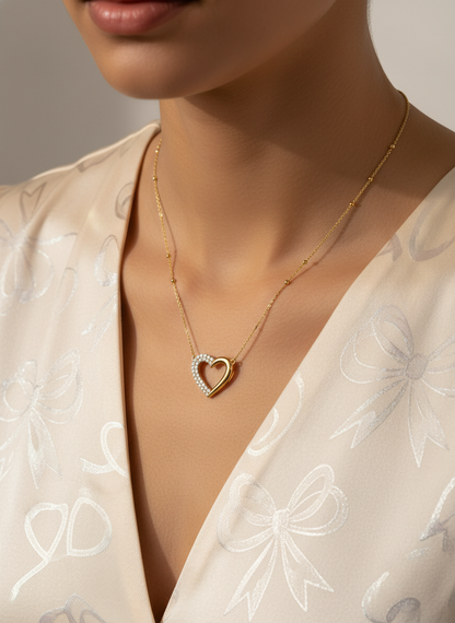 Gold necklace with a heart-shaped pendant worn by a person in a light-colored outfit.