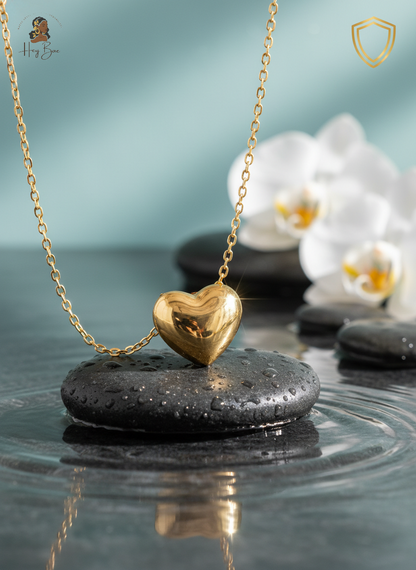 Gold heart-shaped pendant necklace on a black stone with a blurred background of white orchids.