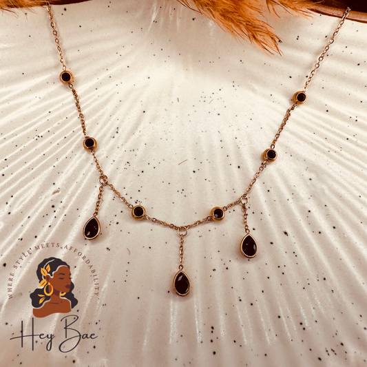 A black and rose gold stainless steel necklace chain with elegant teardrop pendants displayed on a white surface.