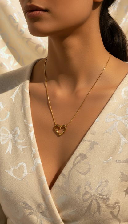 Woman wearing a gold heart-shaped necklace against a neutral background