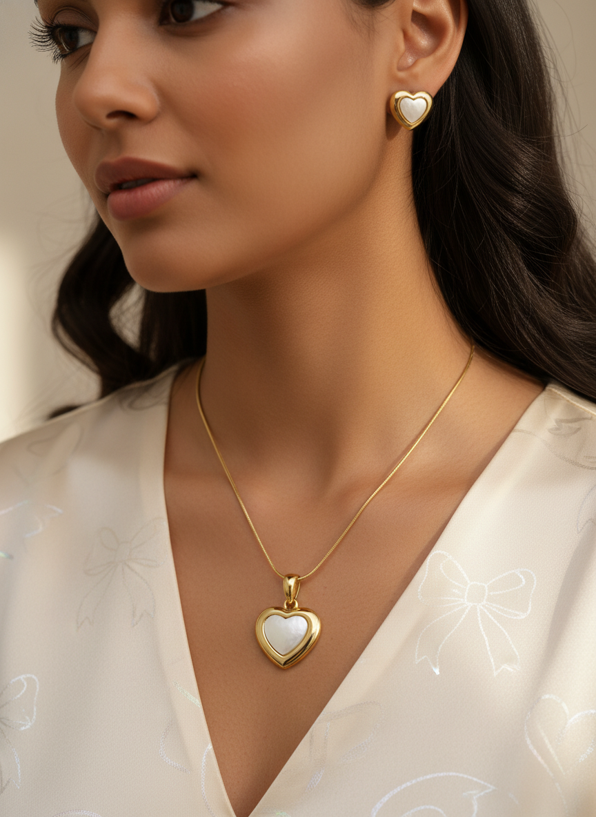 Woman wearing a gold heart-shaped necklace and earrings against a neutral background
