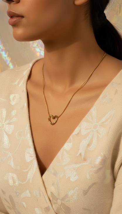 Close-up of a person wearing a gold necklace with a heart pendant, set against a neutral background.