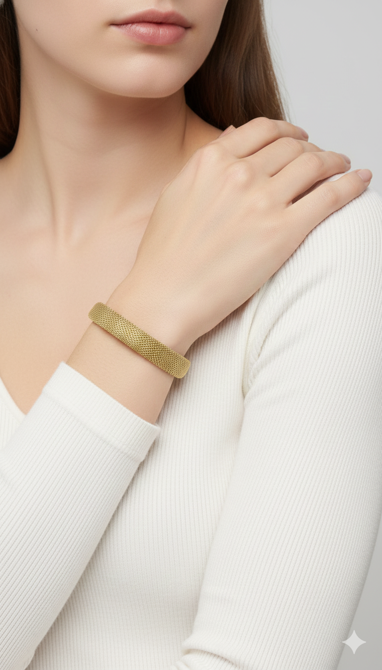 Gold mesh anti tarnish statement bracelet on a person's wrist with a plain background