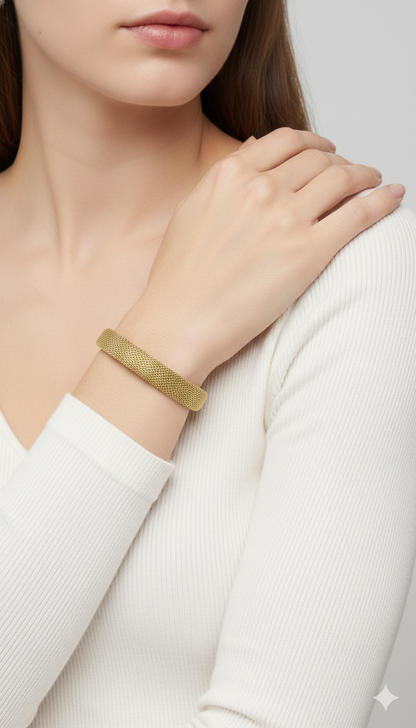 Gold mesh anti tarnish statement bracelet on a person's wrist with a plain background