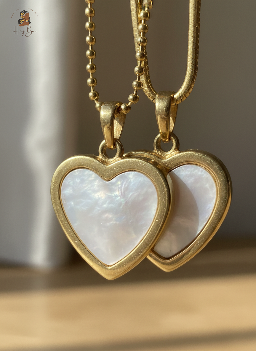 Two gold heart-shaped pendants with white centers on a neutral background