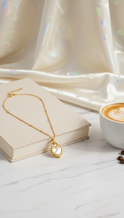 Gold necklace with a heart pendant on a book next to a cup of coffee.
