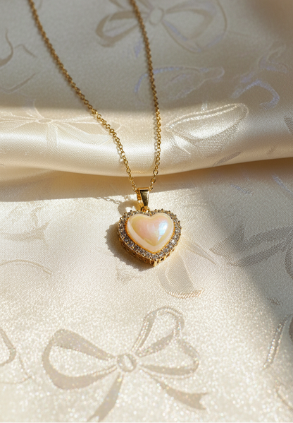 Heart-shaped pearl pendant necklace on a soft fabric background with 'JewelDen' branding.