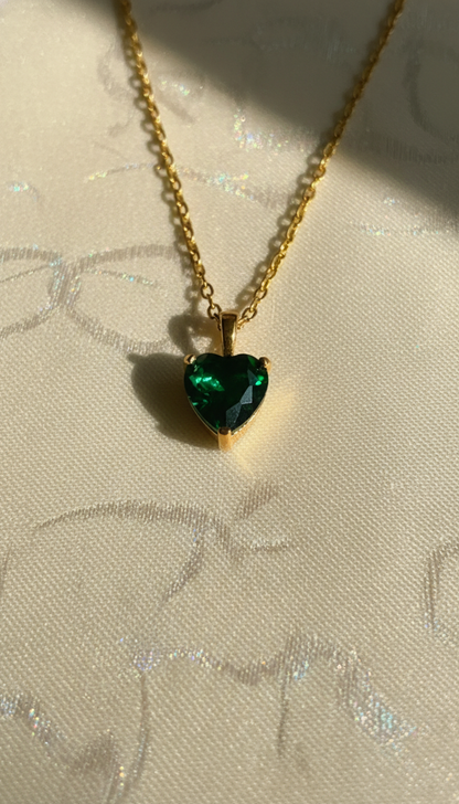 Gold pendant with a green heart-shaped pendant on a textured beige background