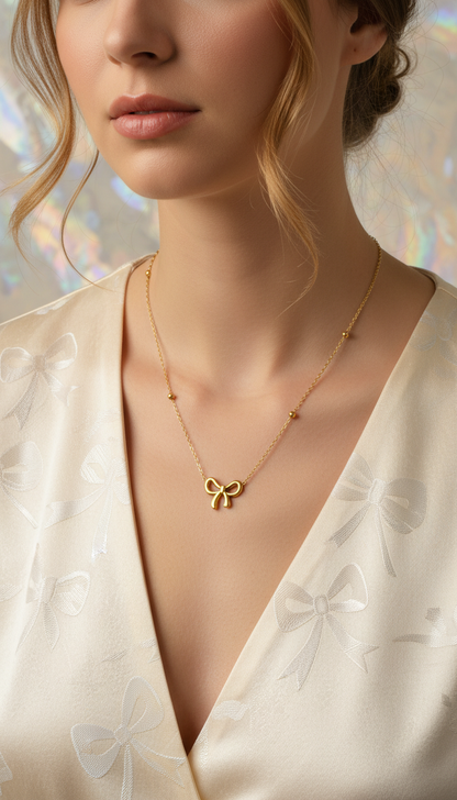 Gold necklace with a bow pendant worn by a model in a white garment.