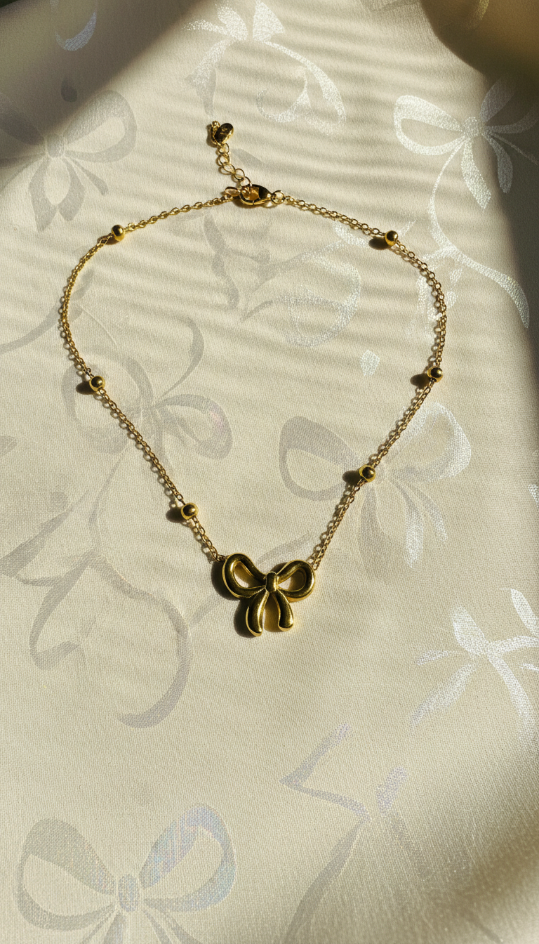 Gold necklace with a bow-shaped pendant on a light floral-patterned fabric background