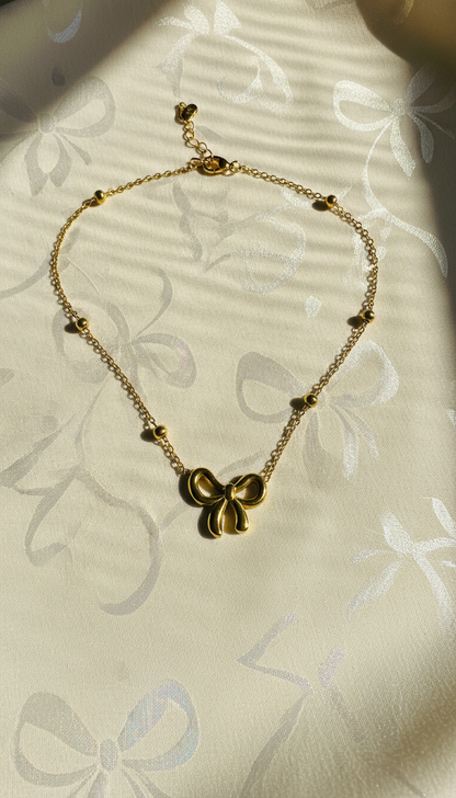Gold necklace with a bow-shaped pendant on a light floral-patterned fabric background