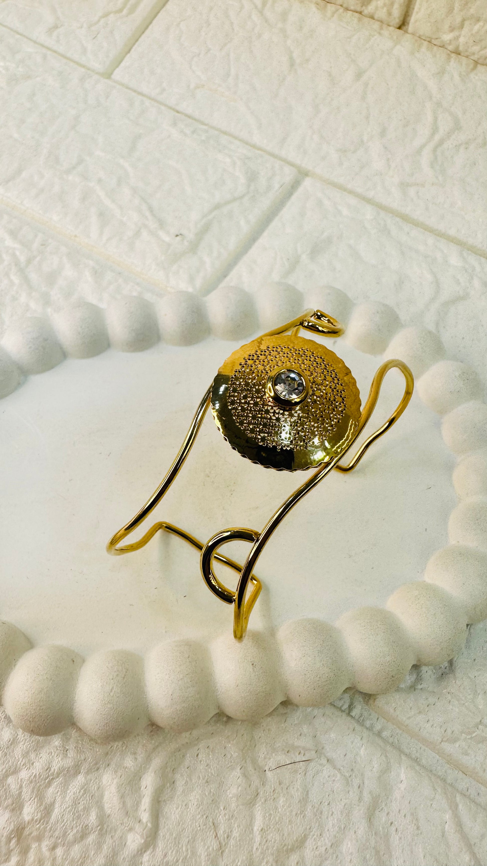 Angled close-up of gold cuff bracelet with textured disc and pearl stone