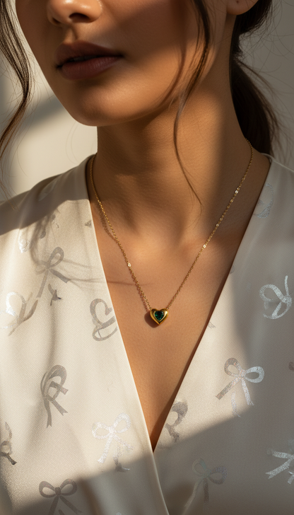 Close-up of a person wearing a gold necklace with a heart-shaped pendant on a white background.