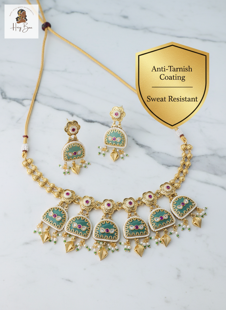 Gold necklace and earrings set with gemstones on a marble background, featuring 'Anti-Tarnish Coating' and 'Sweat Resistant' text.