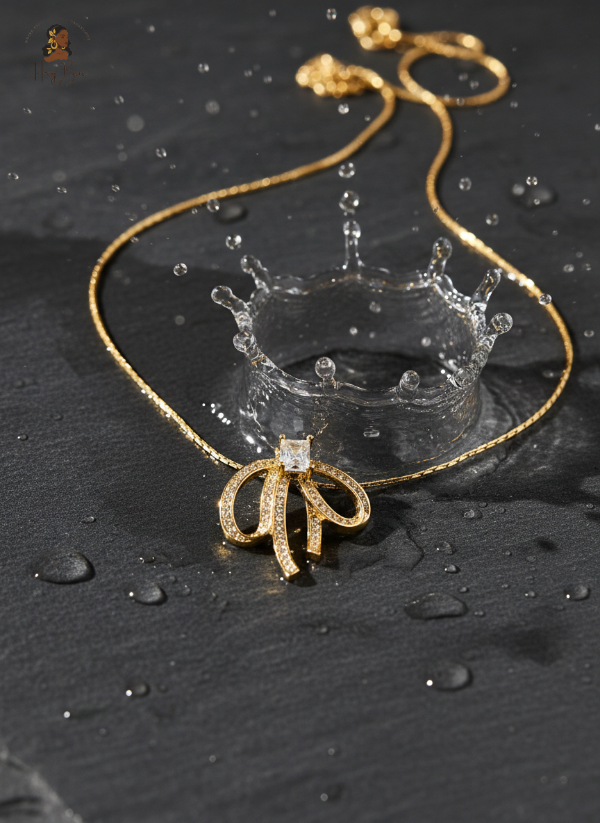 Gold necklace with a bow-shaped pendant on a dark surface with water droplets.