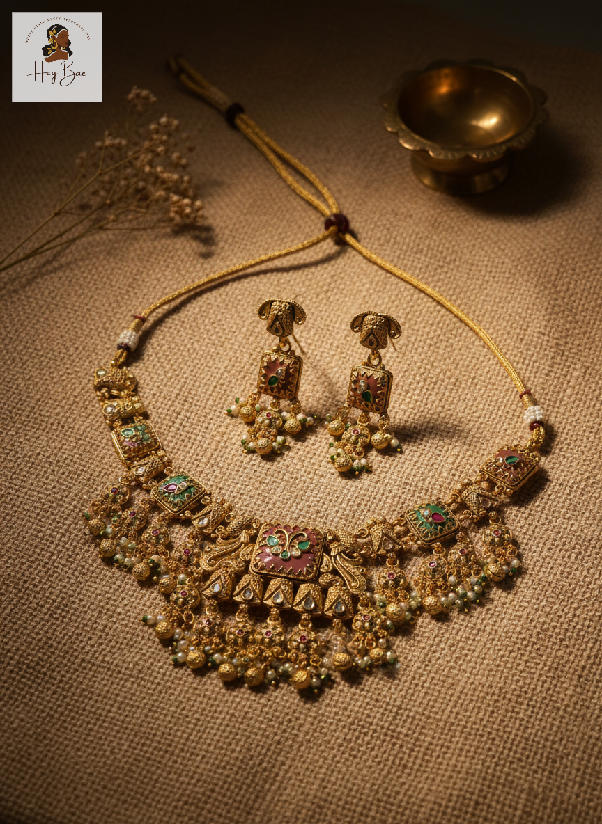 Gold necklace and earrings set on a textured surface with a small bowl and flowers.