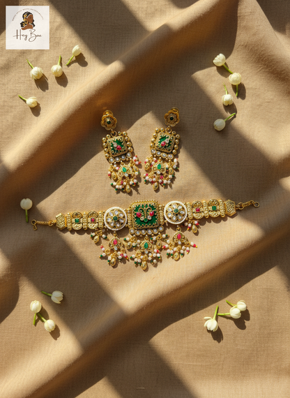 Gold jewelry set with green and red stones on a beige fabric background