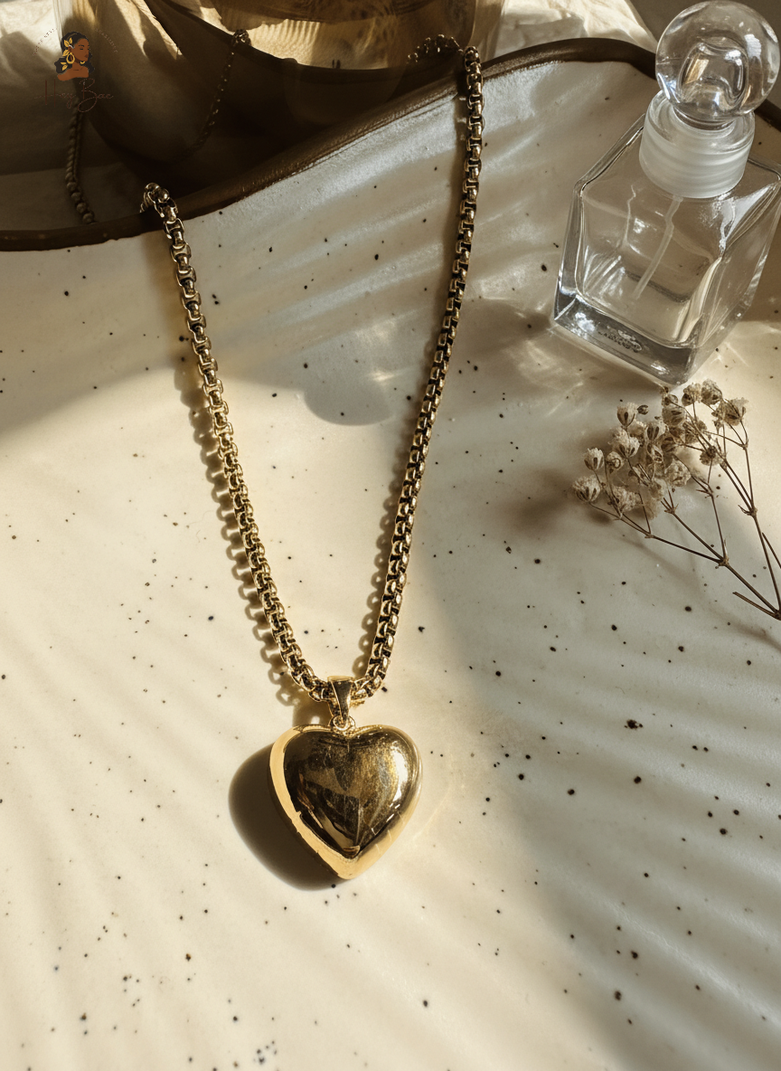 Gold heart-shaped necklace on a textured surface with a bottle and flowers.